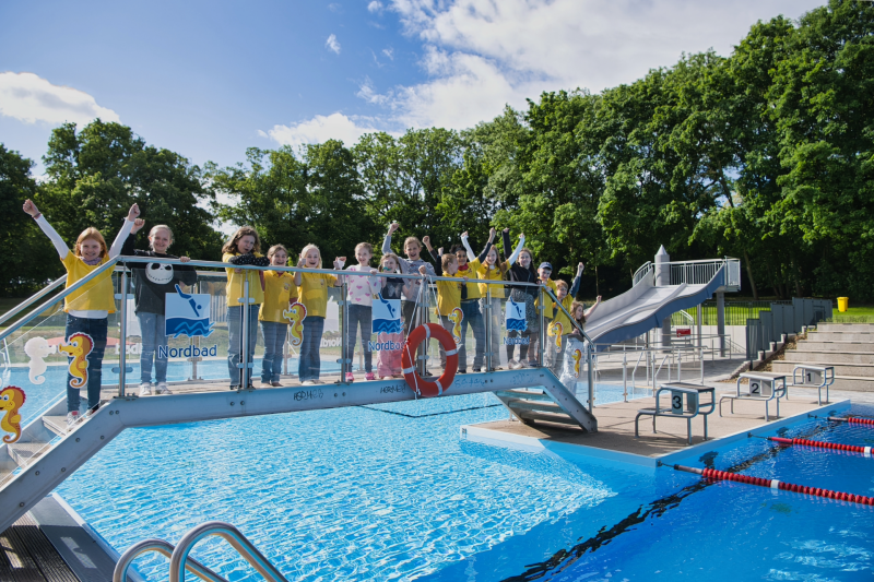 Kinder stehe freudig auf einer Brücke des Freibad Nordbad Halle.