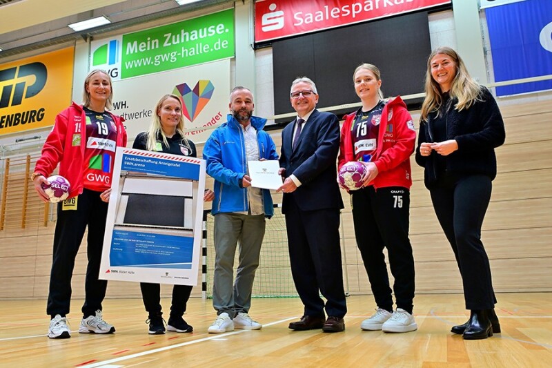 Mitarbeiter übergeben Scheck an Sportlerinnen.