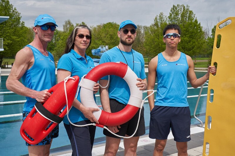 Vier Personen stehen r am Beckenrand und schauen in die Kamera. 
