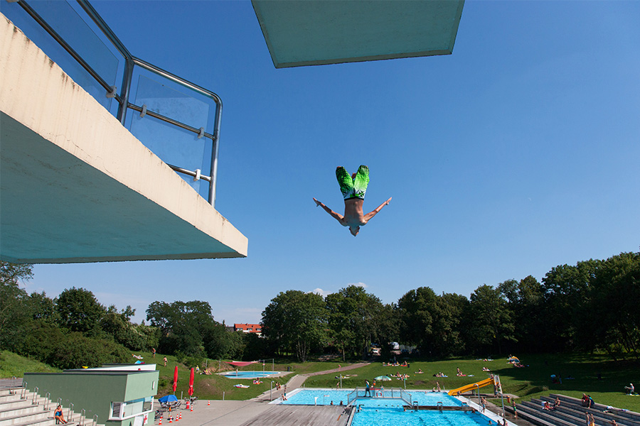 Mann springt von einem Sprungturm in ein Wasserbecken im Freibad Nordbad in Halle (Saale)