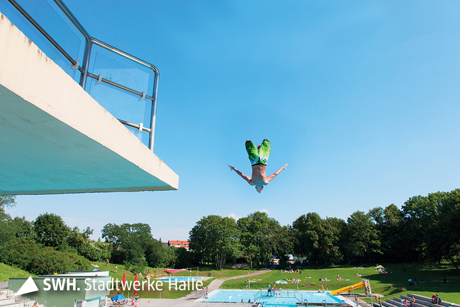 Mann springt von einem Sprungturm in ein Wasserbecken im Freibad Nordbad in Halle (Saale)