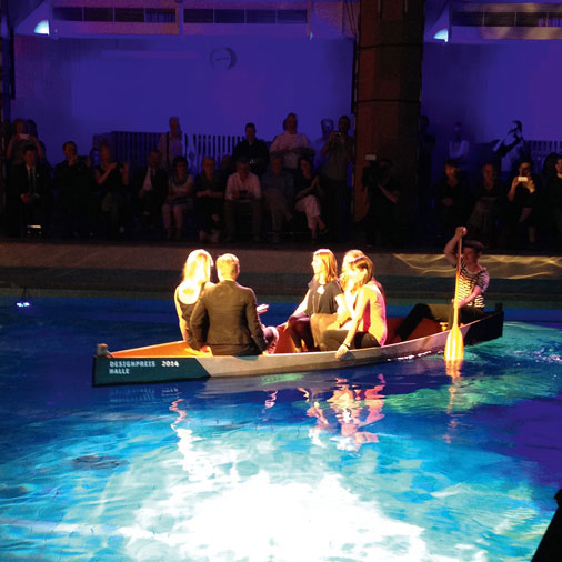 Schauspieler fahren mit einem Boot im Schwimmbecken.