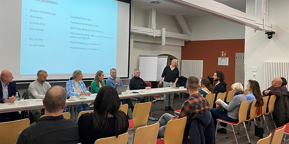 Menschengruppe sitzt vor einer Präsentation. 