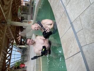 Zwei Männer stehen im Wasserbecken. Die Oberkörper sind nackt. beide halten eine Brille in der Hand, mit der man die virtuelle Wasserwelt erschnorcheln kann.
