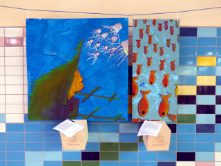 Zwei Bilder hängen an der Wand in der Schwimmhalle Neustadt. Auf ihnen sind Unterwasseraufnahmen gezeichnet.