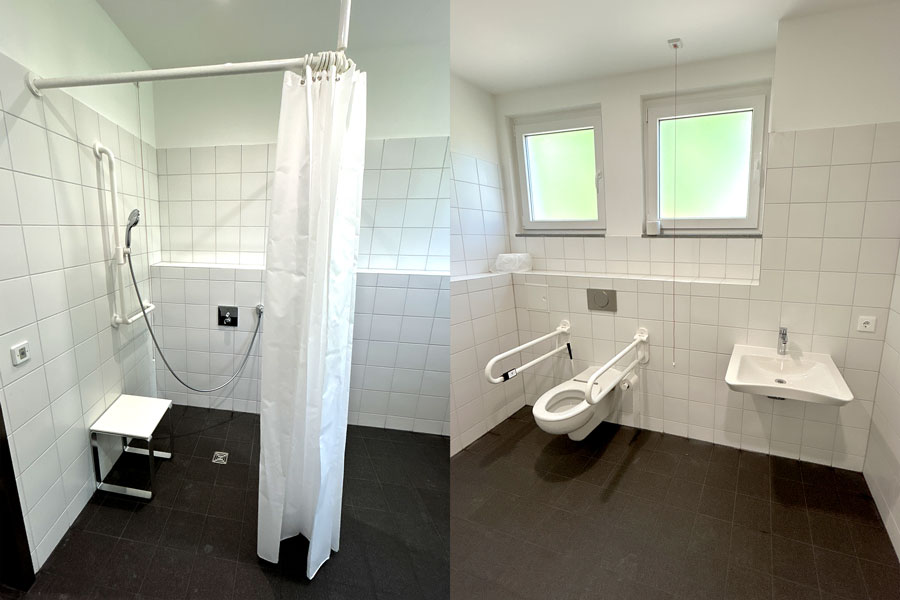 Barrierefreier Sanitärbereich mit Duschvorhang, Duschstuhl, Haltegriffen, wandhängendem WC und Waschbecken unter zwei Kippfenstern