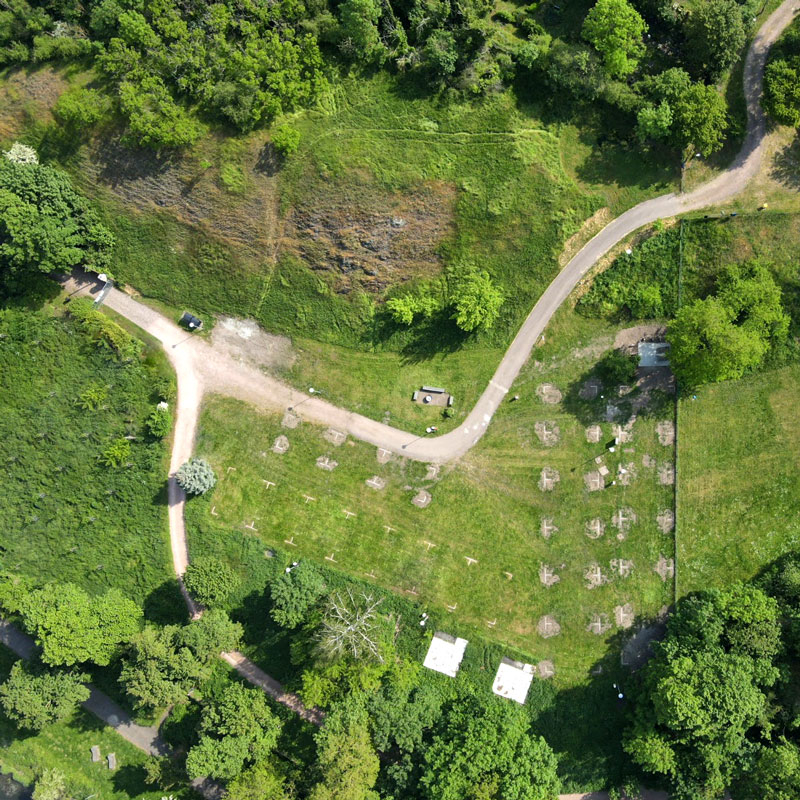Luftaufnahme eines Campingplatzes mit Zeltflächen, Wegen und umgeben von Bäumen