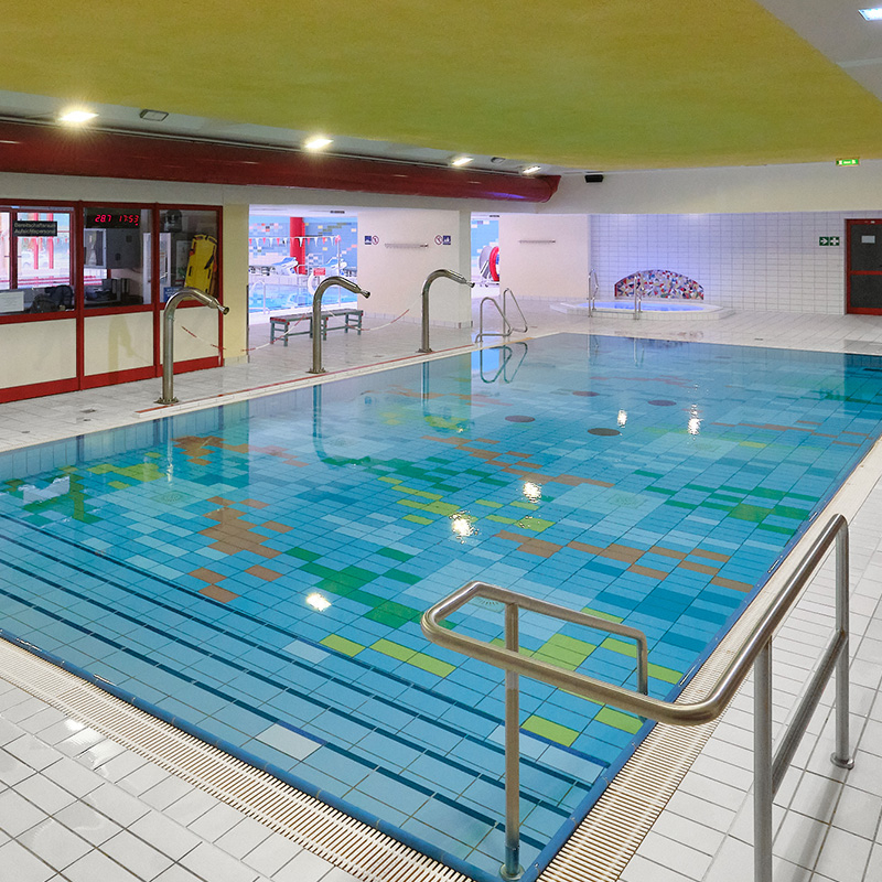 Flaches Kinderbecken der Schwimmhalle Neustadt mit buntem Fliesenboden, Edelstahlhandläufen und Treppen. 