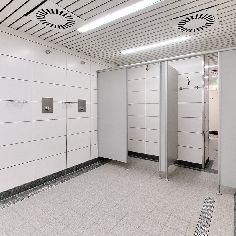 Sanitärbereich der Schwimmhalle Neustadt mit gefliesten Wänden und Boden, Duschen sowie abgetrennten Toilettenkabinen.