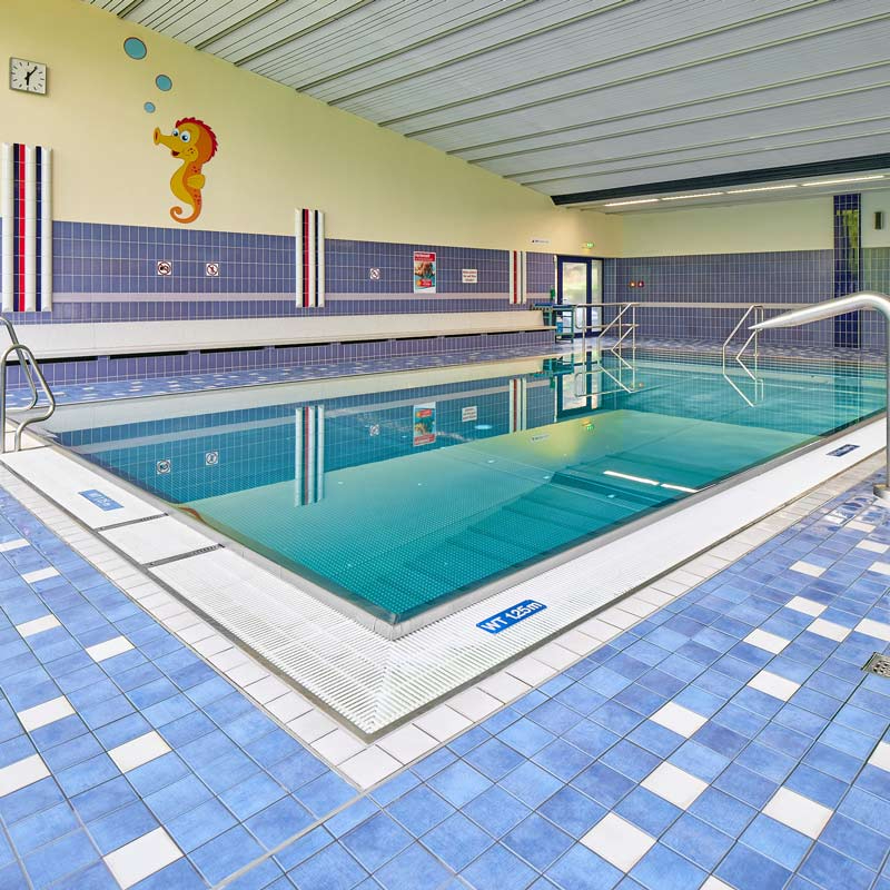 Ansicht eines Schwimmbeckens mit blauen Fliesen, einer Treppe und einer Wanddekoration mit einem Seepferdchen