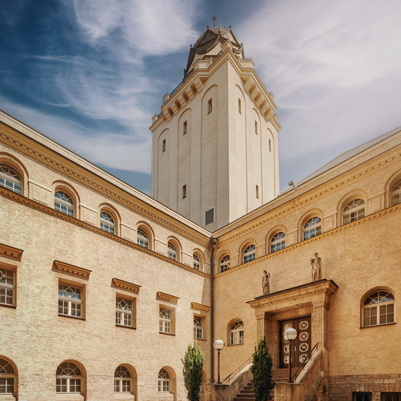 Innenhof des historischen Stadtbades mit hohem Turm, mehreren Fenstern und einer Treppe am Eingang