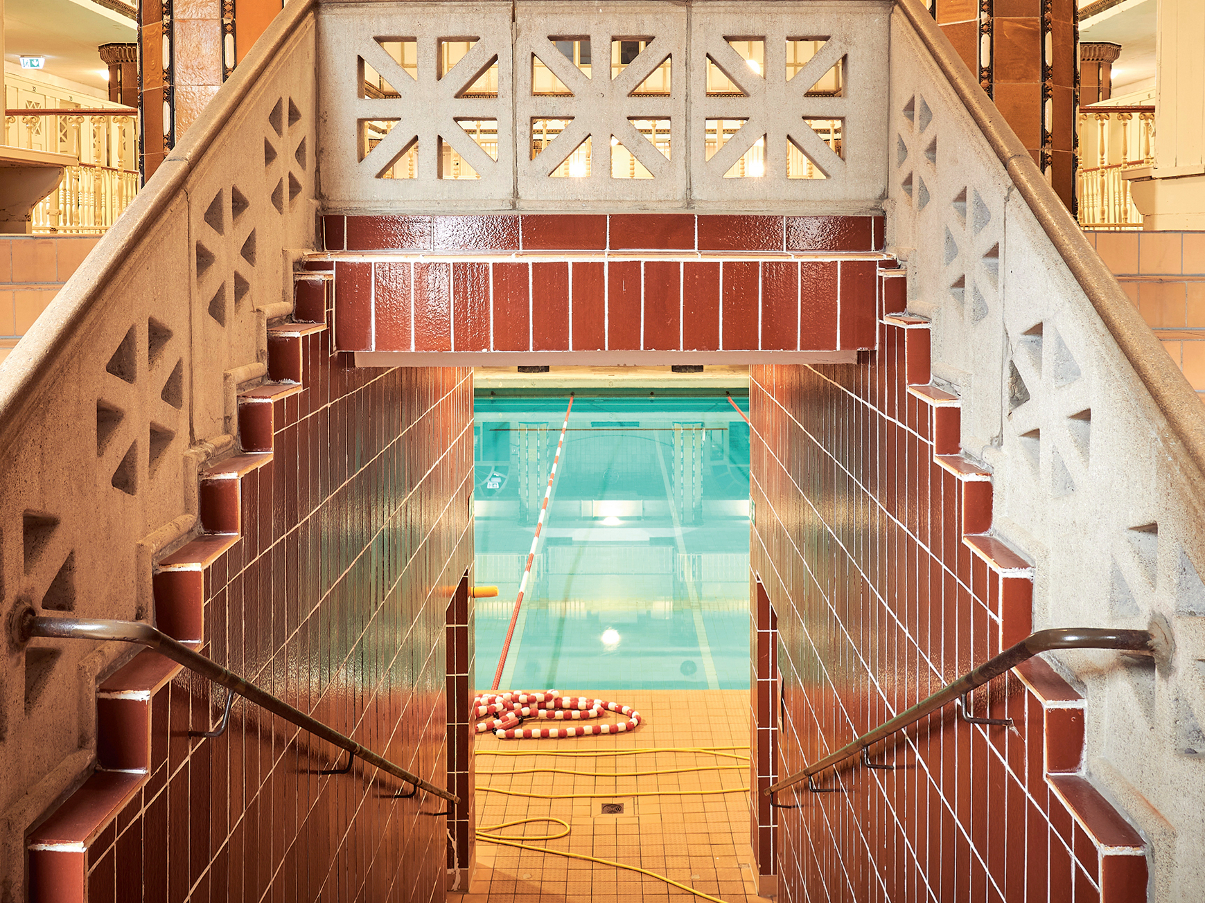 Ein Blick durch die Tür der Männerhalle auf das große Schwimmbecken, links und rechts des Durchgangs führen Treppen nach oben.